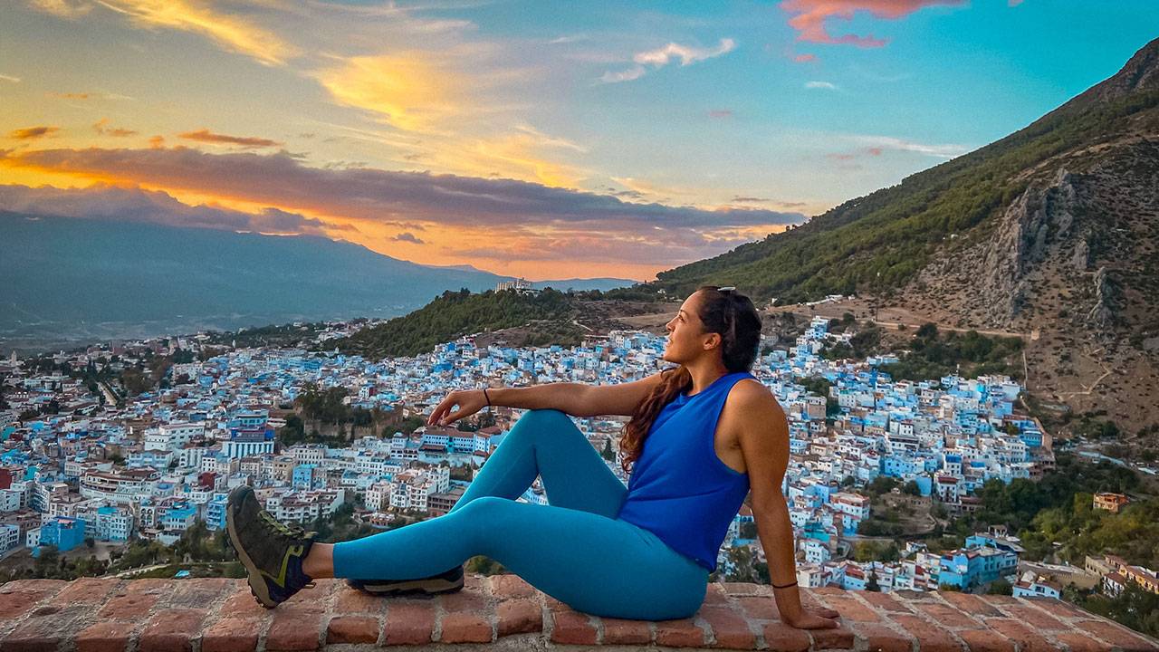 Woman in blue activewear relaxing on brick wall overlooking blue cityscape at sunset
