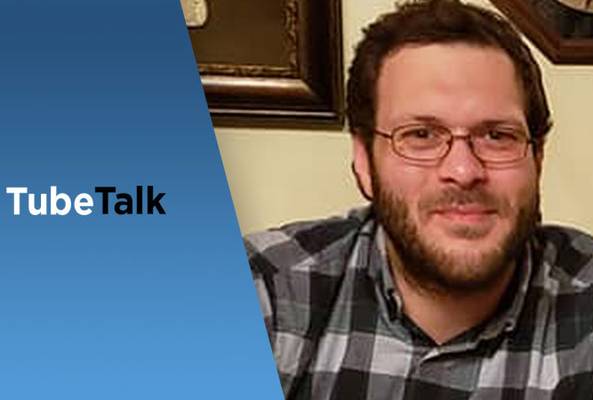 Man in glasses smiling next to blue panel with TubeTalk logo for video podcast.