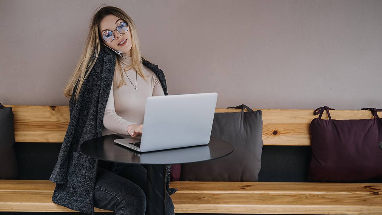 Young woman working on laptop while talking on smartphone in modern cafe setting