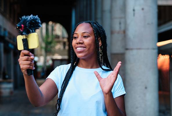 Young woman recording vlog with smartphone and microphone in urban outdoor setting