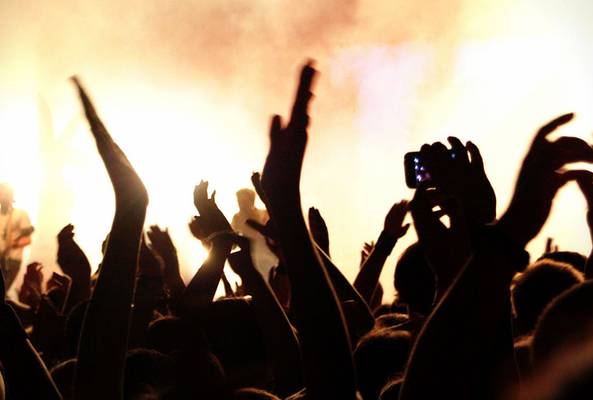 Silhouettes of concert crowd with raised hands and bright stage lights in background