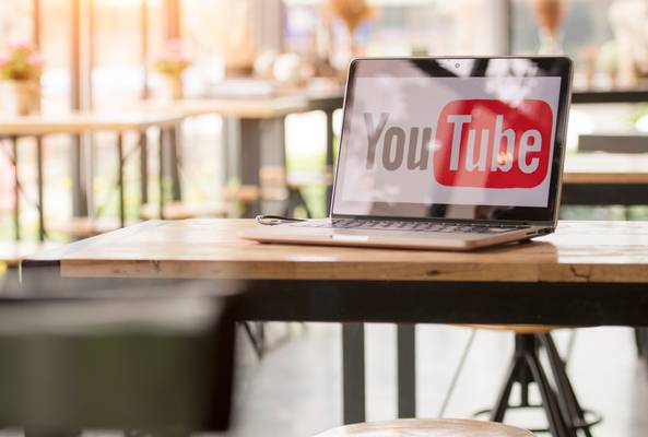 Laptop on wooden table displaying YouTube logo in a bright, modern workspace