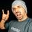 Man in gray beanie and shirt making rock hand sign with open mouth expression against black background