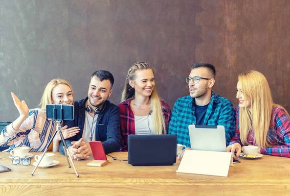 Group of young adults recording a video podcast with laptops, smartphones, and coffee cups.