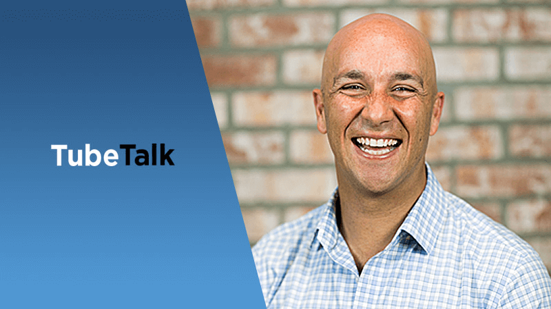 Smiling bald man in checkered shirt beside blue panel with TubeTalk logo text