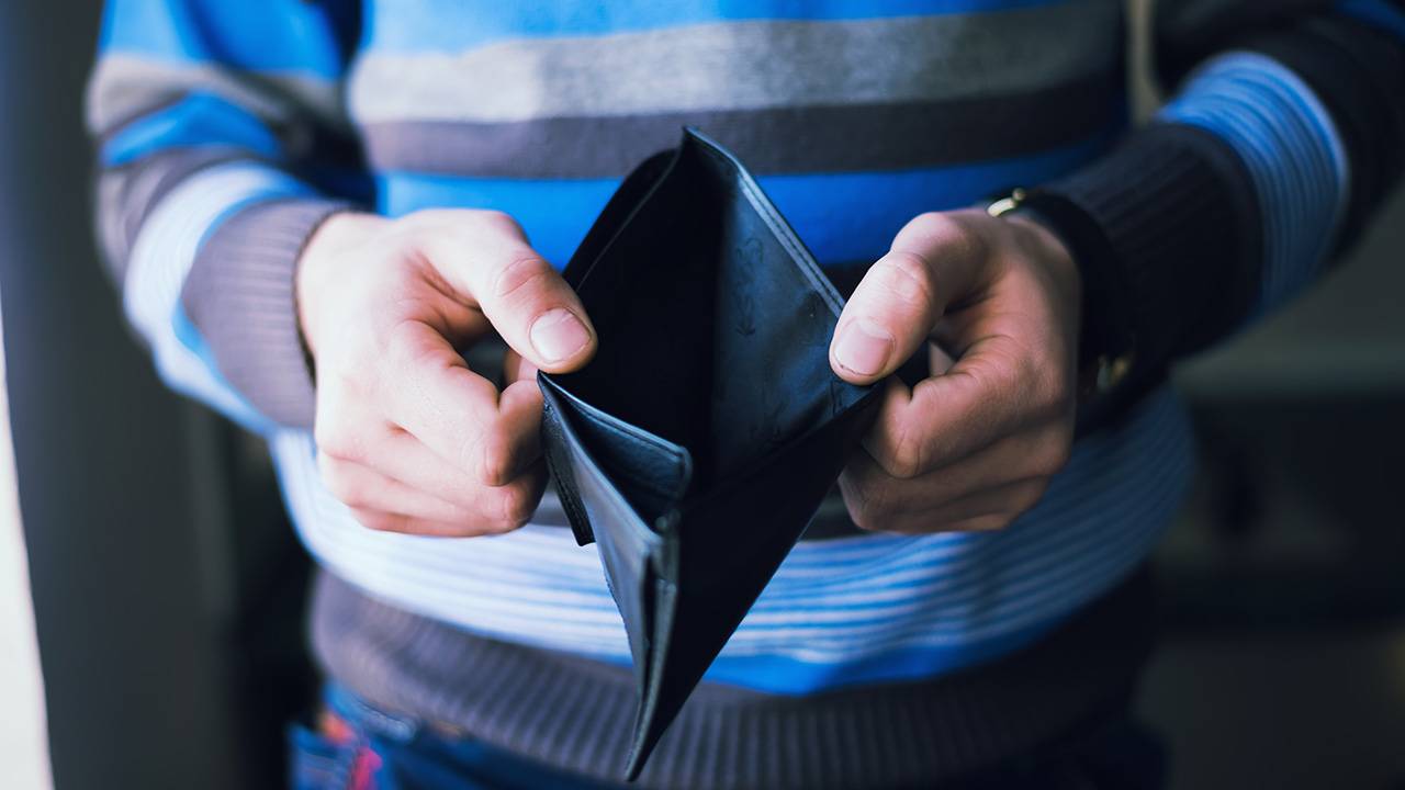 Person holding an empty black wallet symbolizing financial hardship or lack of cash.