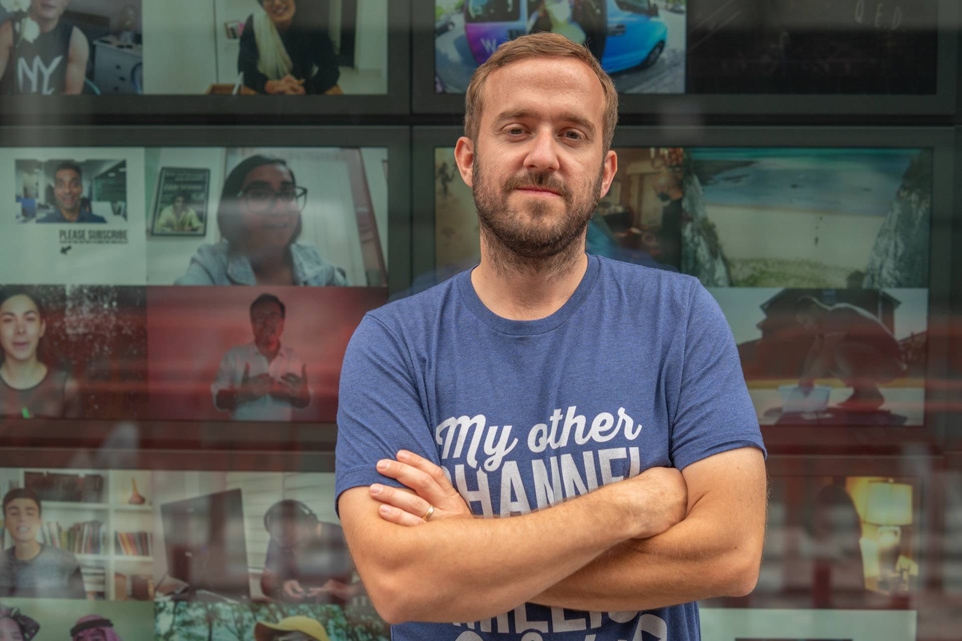 Man in casual t-shirt standing with arms crossed in front of video call screen wall