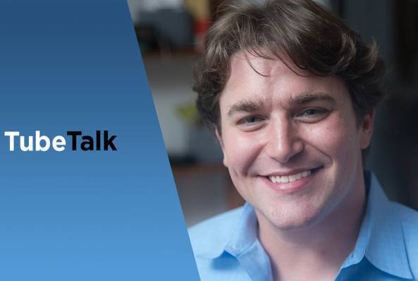 Smiling man in blue shirt beside blue banner with TubeTalk logo for video podcast.