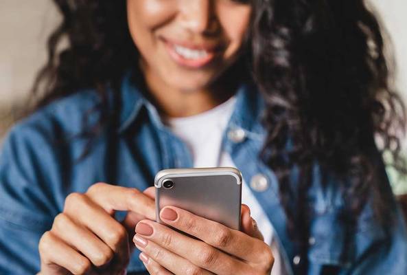 Woman smiling while using smartphone, browsing or texting in casual denim jacket.