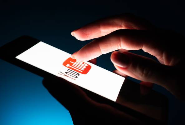 Hand holding smartphone with YouTube app logo on screen in dark environment