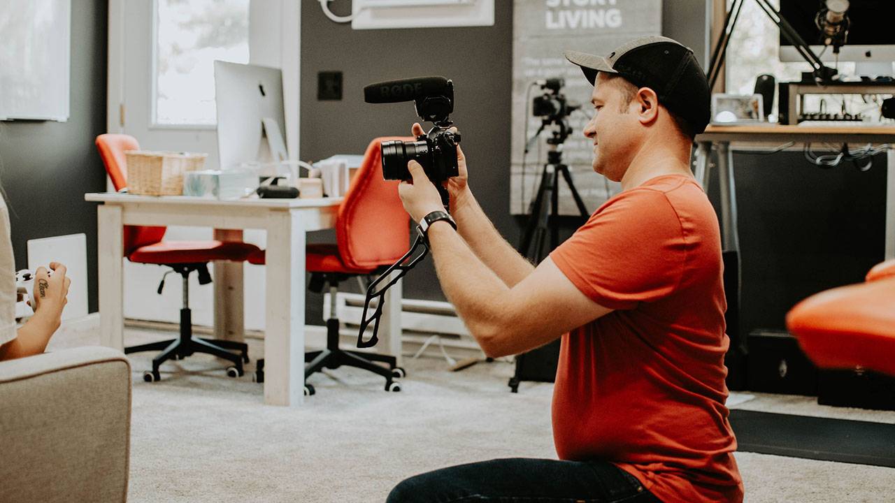 Man in red shirt filming with camera in modern office environment with equipment