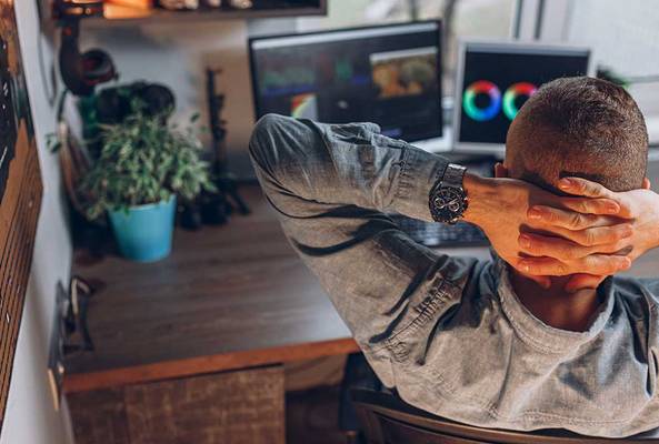Man relaxing at desk with multiple screens, color grading video editing software visible