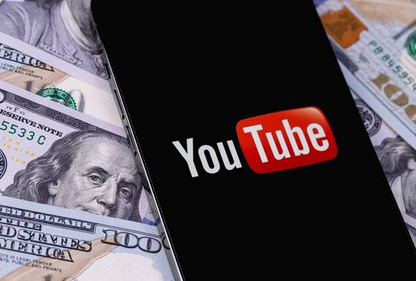 YouTube logo displayed on smartphone screen over US hundred dollar bills background.