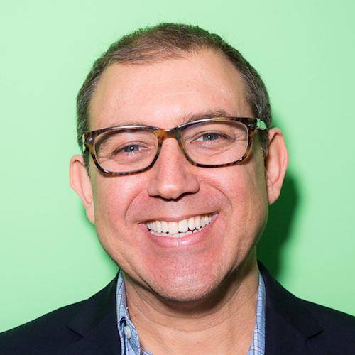 Smiling man wearing glasses and business casual attire with a green background.