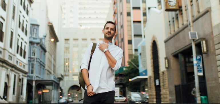Young man with backpack walking confidently on city street in casual white shirt