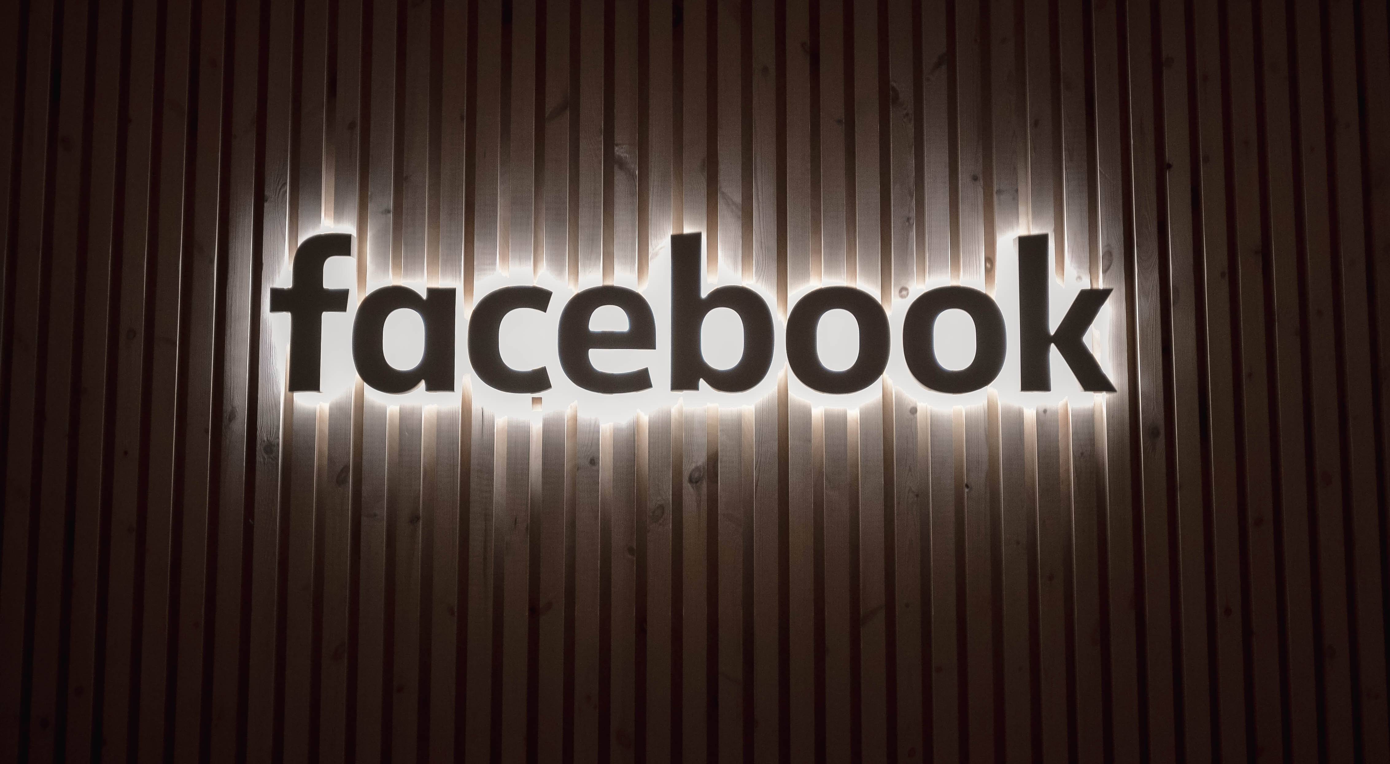 Illuminated Facebook logo sign on a dark wooden slat wall background, social media branding.