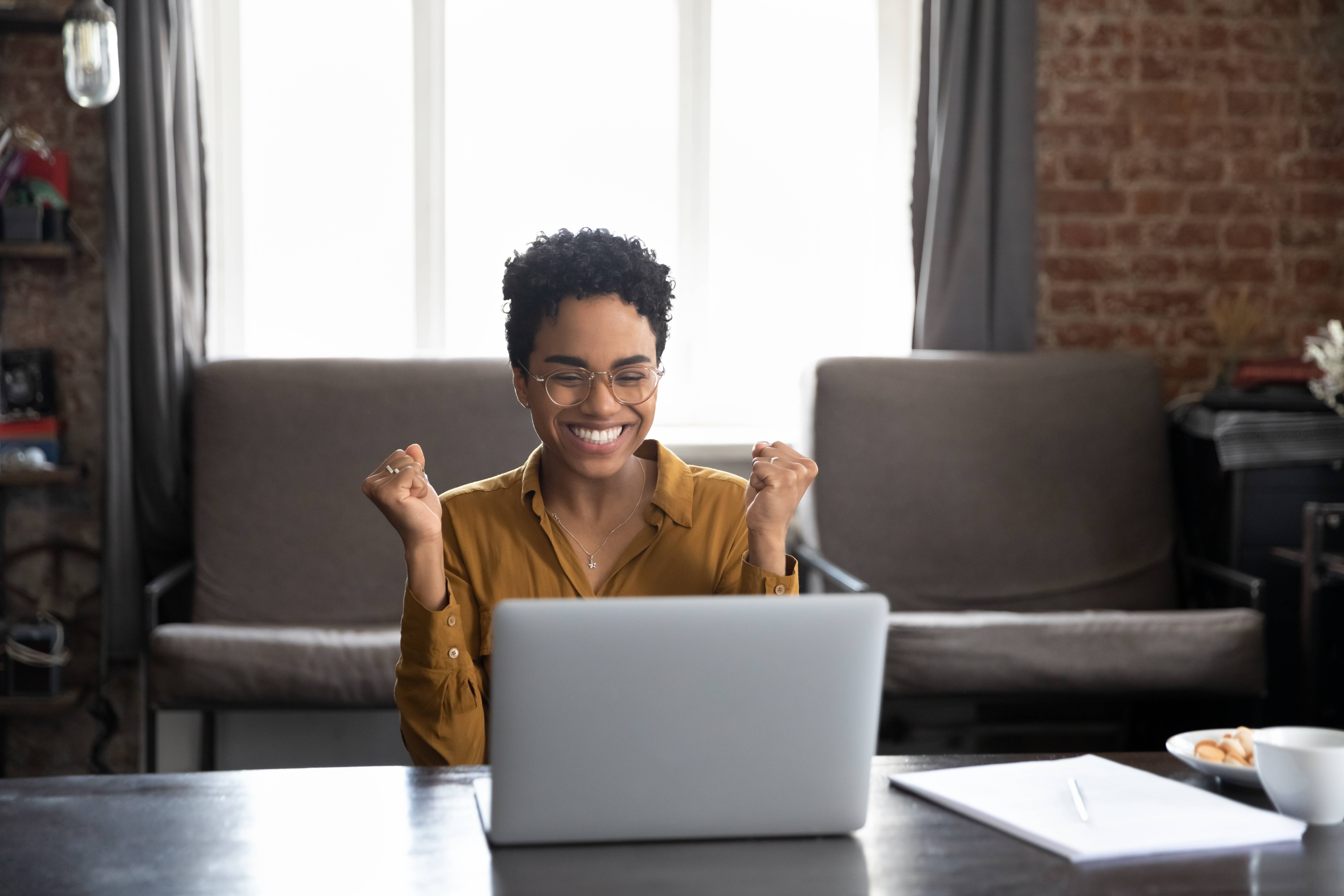 Woman celebrating while looking at laptop