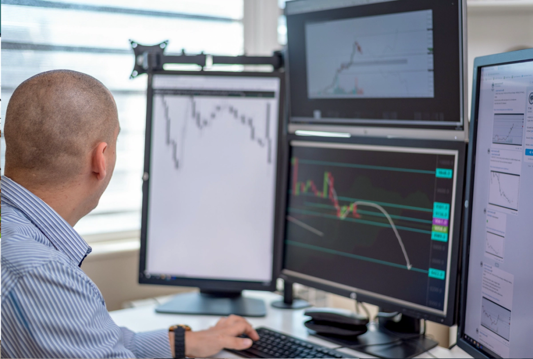 a guy trading stocks on numerous screens inside an office