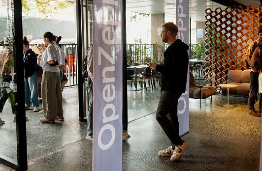 Modern lobby with guests entering through glass doors, stylized column signage, and contemporary lounge seating area visible.