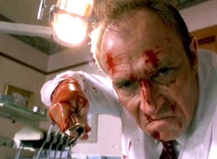 Injured man with blood on his face in a medical setting holding a surgical instrument.