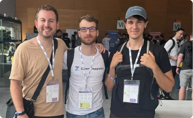 Three men wearing event badges stand together at a conference or trade show venue.
