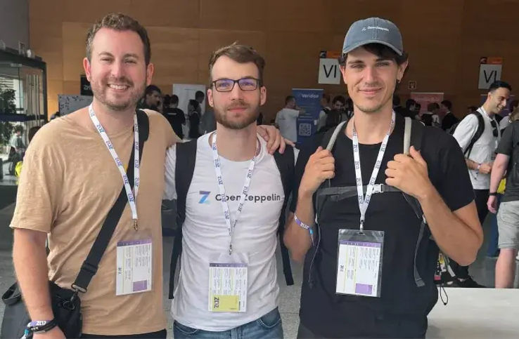 Three men wearing event badges stand together at a conference or trade show venue.