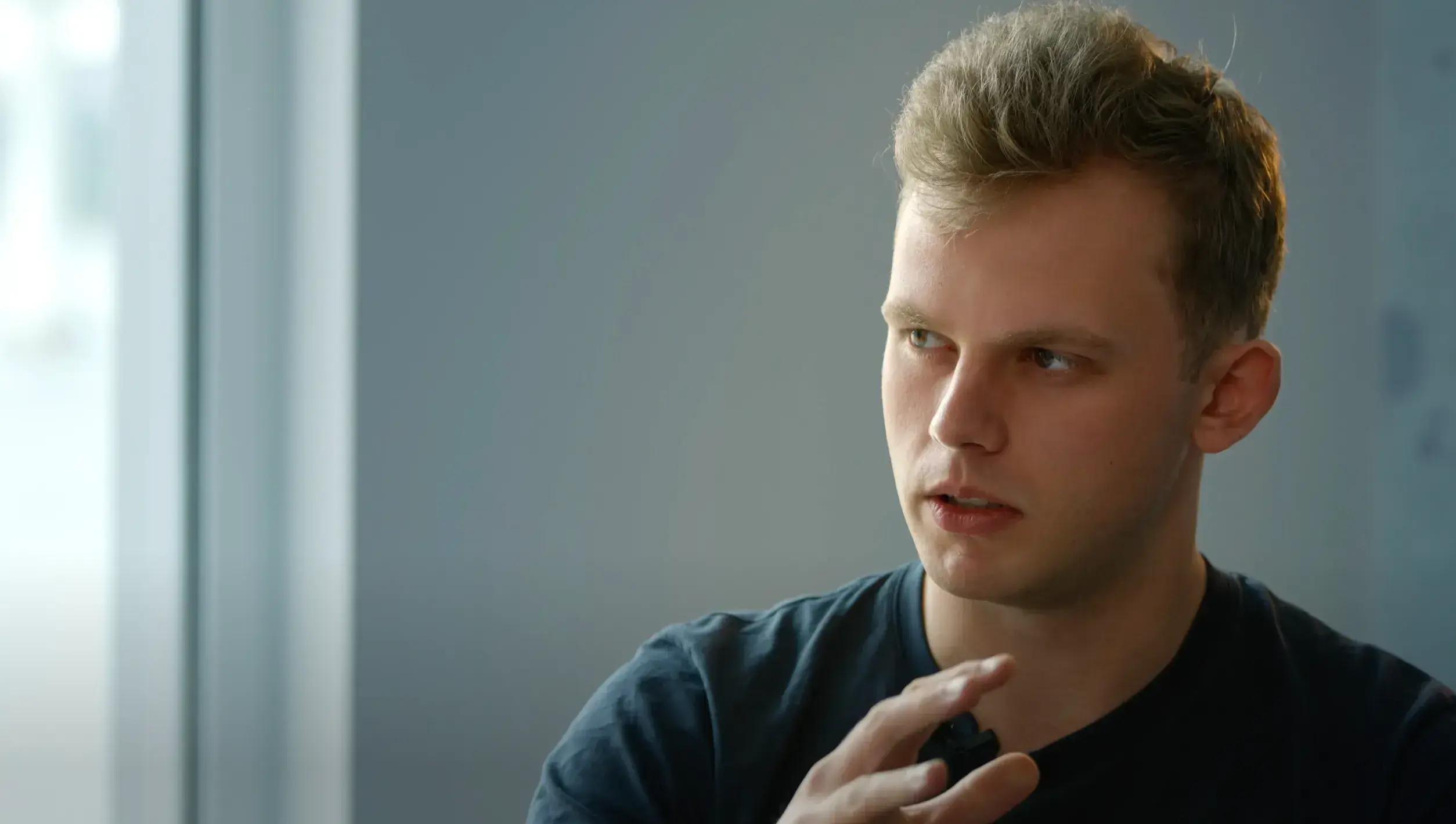 Young man in dark shirt looking thoughtfully to the side in modern office setting.