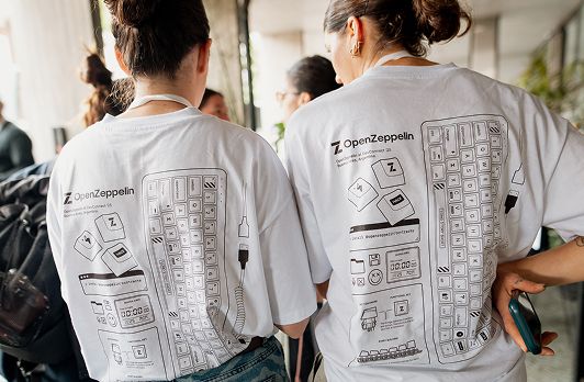 Two people wearing matching OpenZeppelin t-shirts with technical diagram designs printed on the back.