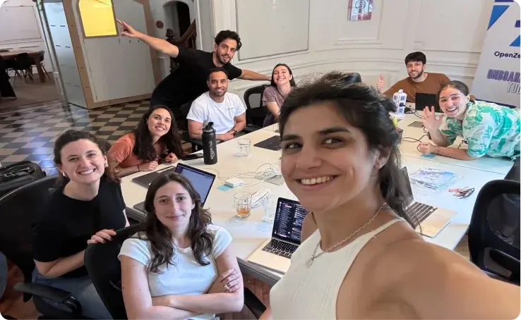 A diverse team of young professionals smiling and posing together around a table in a collaborative workspace.