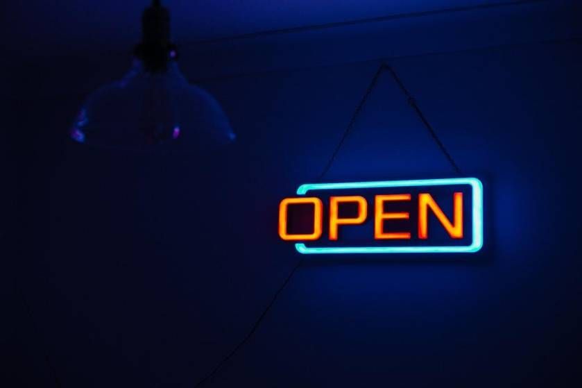 Glowing neon "OPEN" sign in orange and cyan against a dark blue background with silhouetted figure.