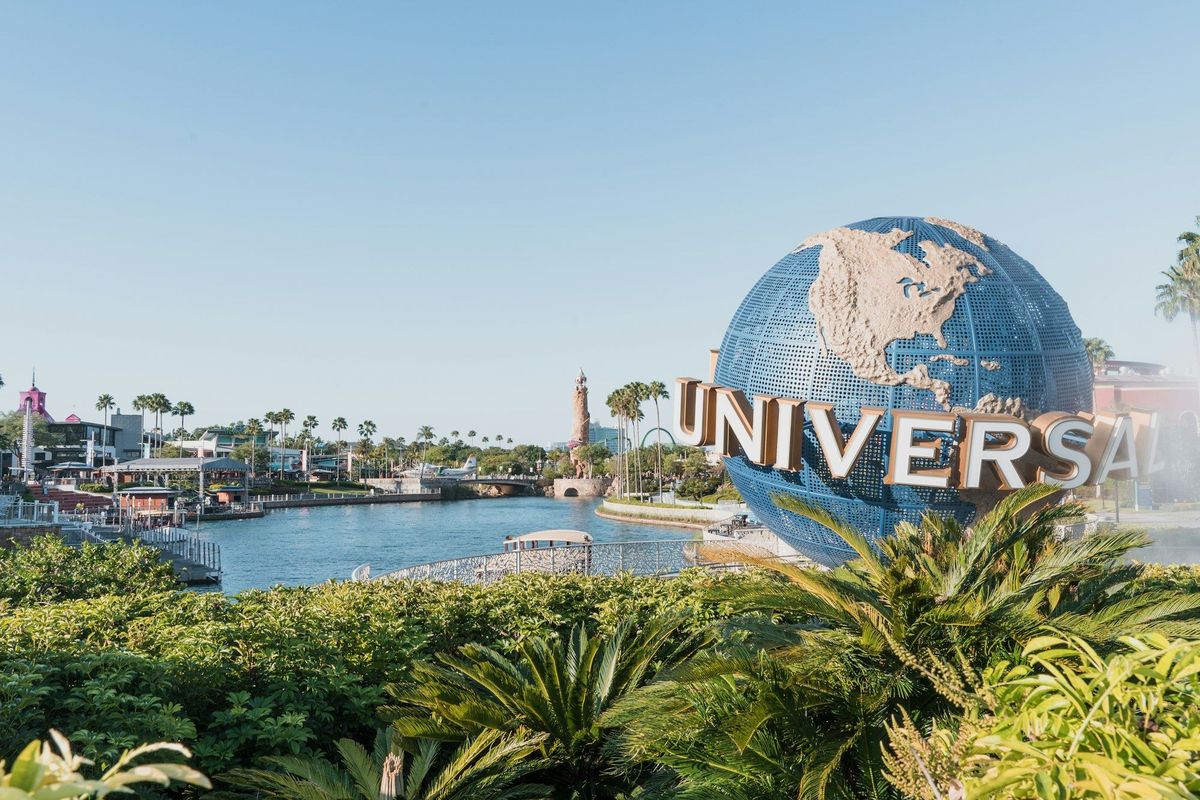 A vibrant view of the Universal Studios theme park featuring the iconic globe sign. The scene captures the lush greenery surrounding the waterway and attractions, conveying a sunny and inviting atmosphere.