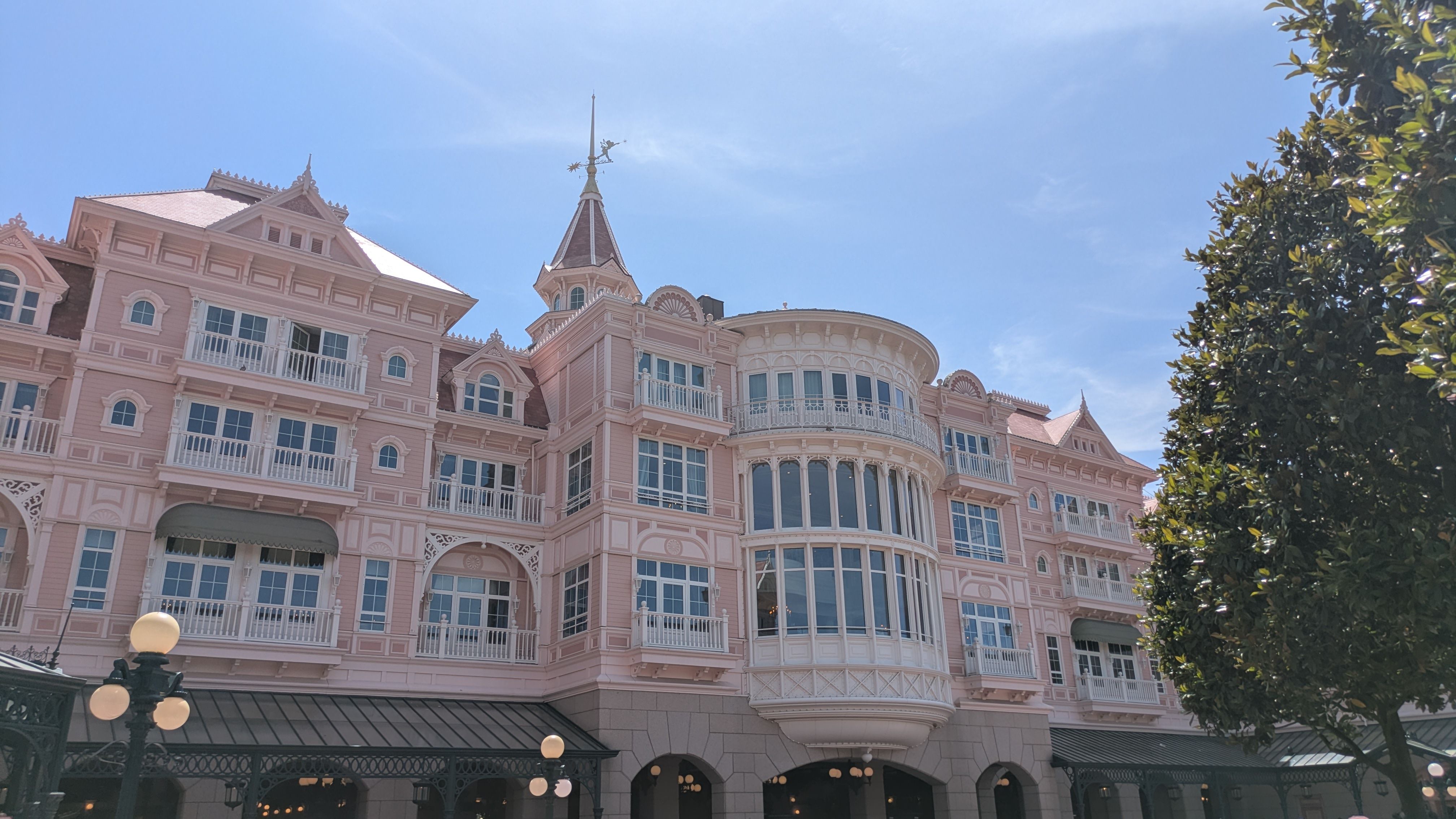 The image captures a large, intricately designed hotel building with a pink façade and Victorian architectural elements. The sky is clear, and the building is adorned with balconies and decorative features typical of a resort setting.