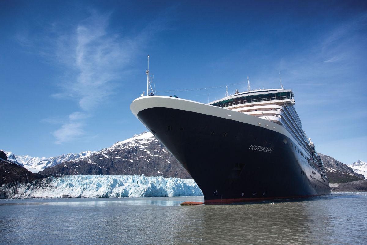 The image depicts a large cruise ship named 'OOSTERDAM' anchored in a serene glacial bay. Snow-capped mountains and a glacier are visible in the background, reflecting a clear blue sky.
