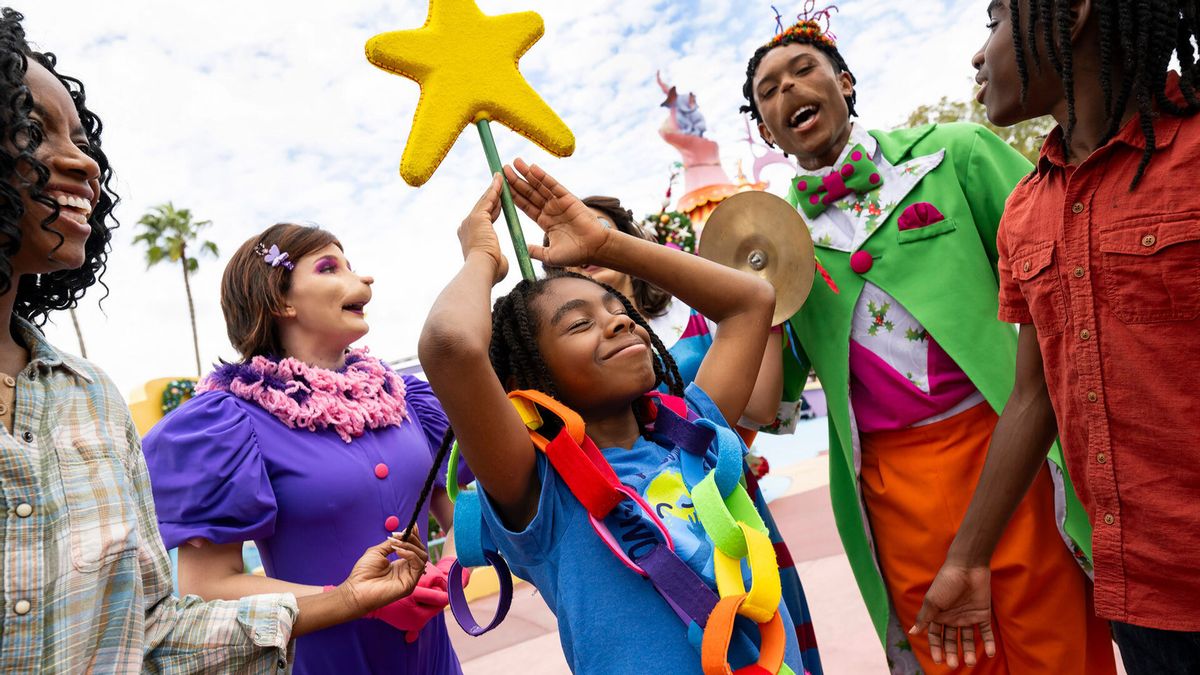 The image captures a joyful moment at a theme park where a child, wearing a colorful outfit, is playfully engaging with performers dressed in vibrant costumes. The scene is filled with smiles and celebration, showcasing an entertaining atmosphere.