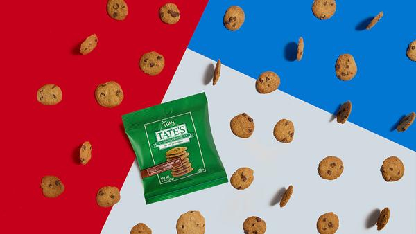 The image features a package of Tate's cookies prominently displayed against a background divided into red and blue sections, with scattered cookies surrounding the package. The arrangement creates a visually appealing contrast that draws attention to the product.