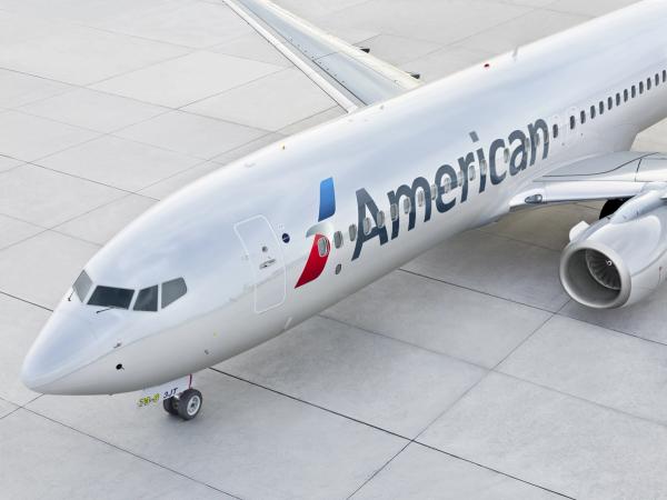 A close-up view of an American Airlines aircraft on a tarmac, showcasing its sleek design and branding. The airplane is parked, highlighting its fuselage and wing structure.