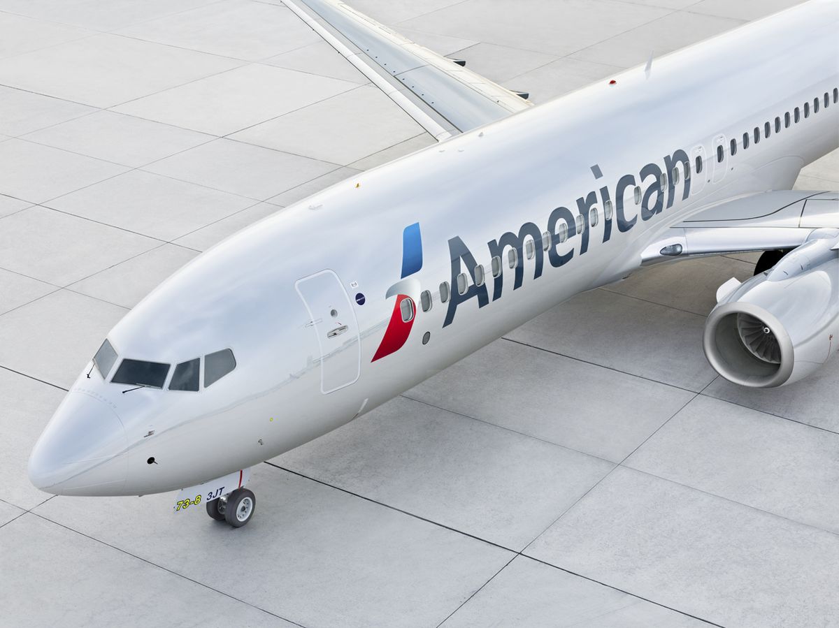 A close-up view of an American Airlines aircraft on a tarmac, showcasing its sleek design and branding. The airplane is parked, highlighting its fuselage and wing structure.