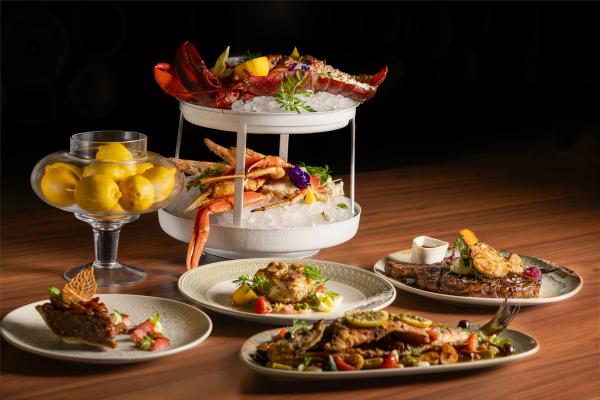 A beautifully arranged seafood platter featuring a variety of shellfish and fish dishes, served on a two-tiered stand with ice. Accompanying the seafood are side dishes presented on elegant plates, completing the gourmet experience.