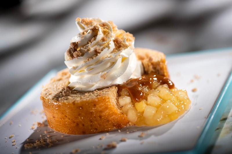 The image showcases a slice of baumkuchen, a traditional German cake, elegantly presented on a white plate. It is topped with whipped cream and a smear of apple compote, creating a visually appealing dessert.