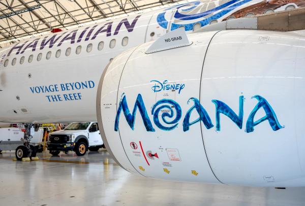 The image features a close-up view of an aircraft's engine with the Disney Moana logo prominently displayed. In the background, a Hawaiian Airlines plane can be seen, which indicates a setting within an airport hangar.