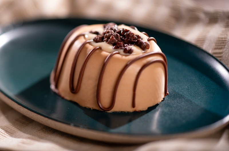 The image features a dessert item, specifically a chocolate mousse, presented elegantly on a plate. The mousse is elegantly drizzled with chocolate and topped with a garnish, giving it a refined appearance.