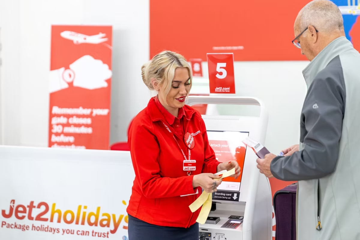 A customer service representative at a travel agency is assisting a client with documentation and providing information. The setting features a bright interior with promotional signage.