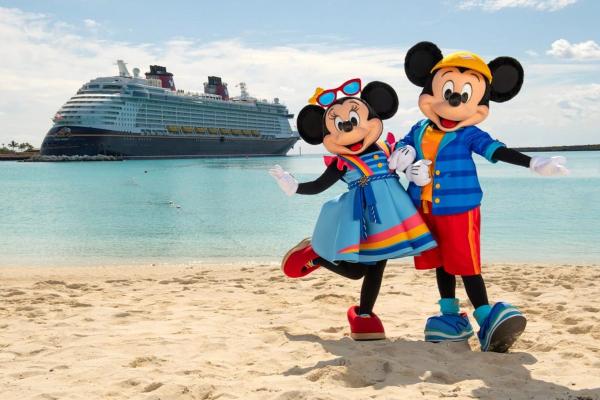 Mickey Mouse and Minnie Mouse pose on a beach with a Disney cruise ship in the background. The scene is bright and colorful, suggesting a festive atmosphere.