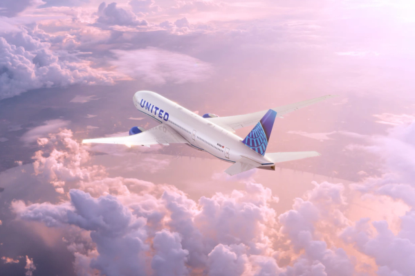 An airplane belonging to United Airlines is shown flying above a sea of clouds during a vibrant sunset. The aircraft is captured in mid-flight, showcasing its design against a colorful sky.