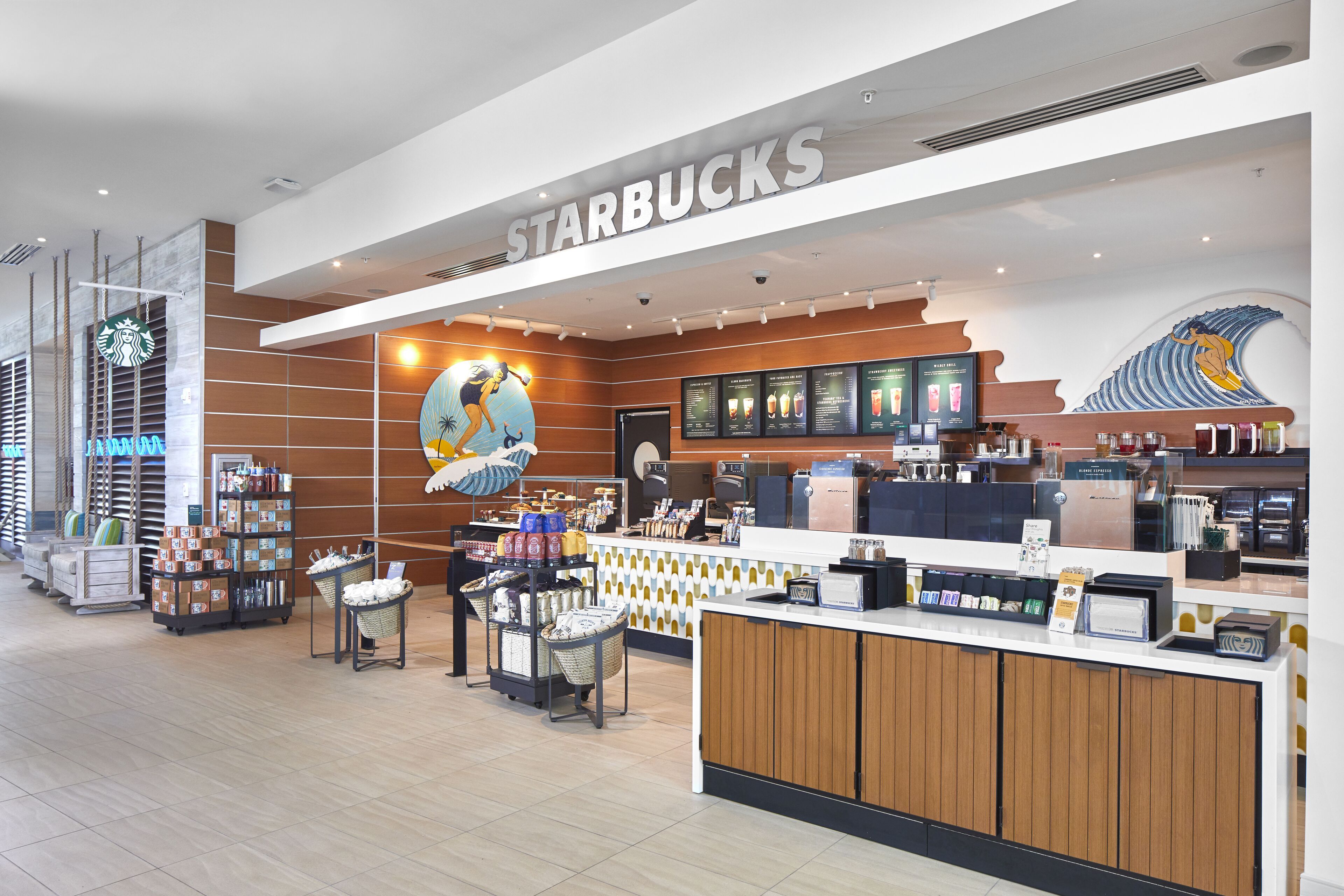 The image features the interior of a Starbucks store, showcasing a modern design with colorful artwork and a service counter. The layout includes seating arrangements and product displays, emphasizing a welcoming atmosphere for customers.