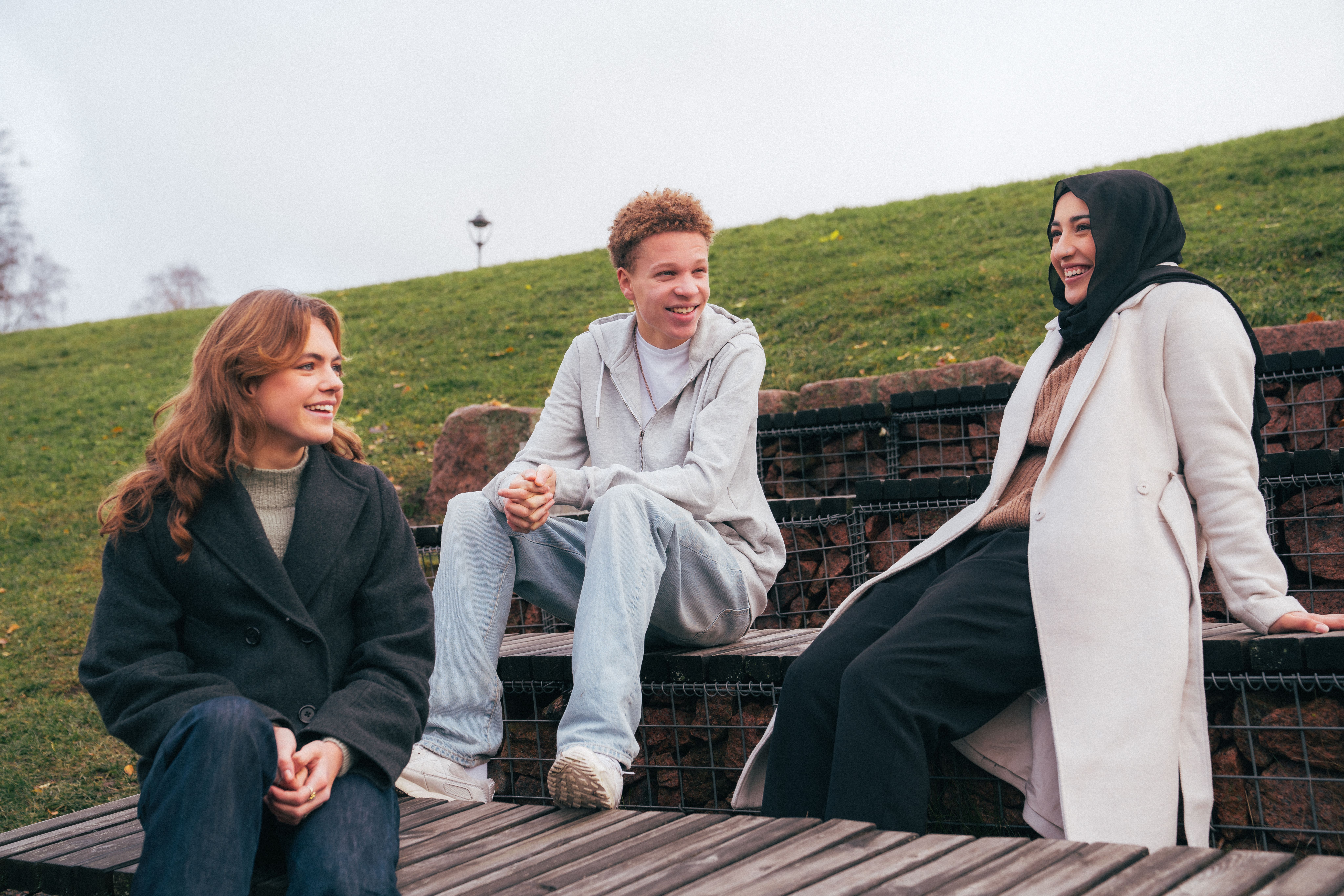 Tre ungdommer snakker og ler sammen i en park
