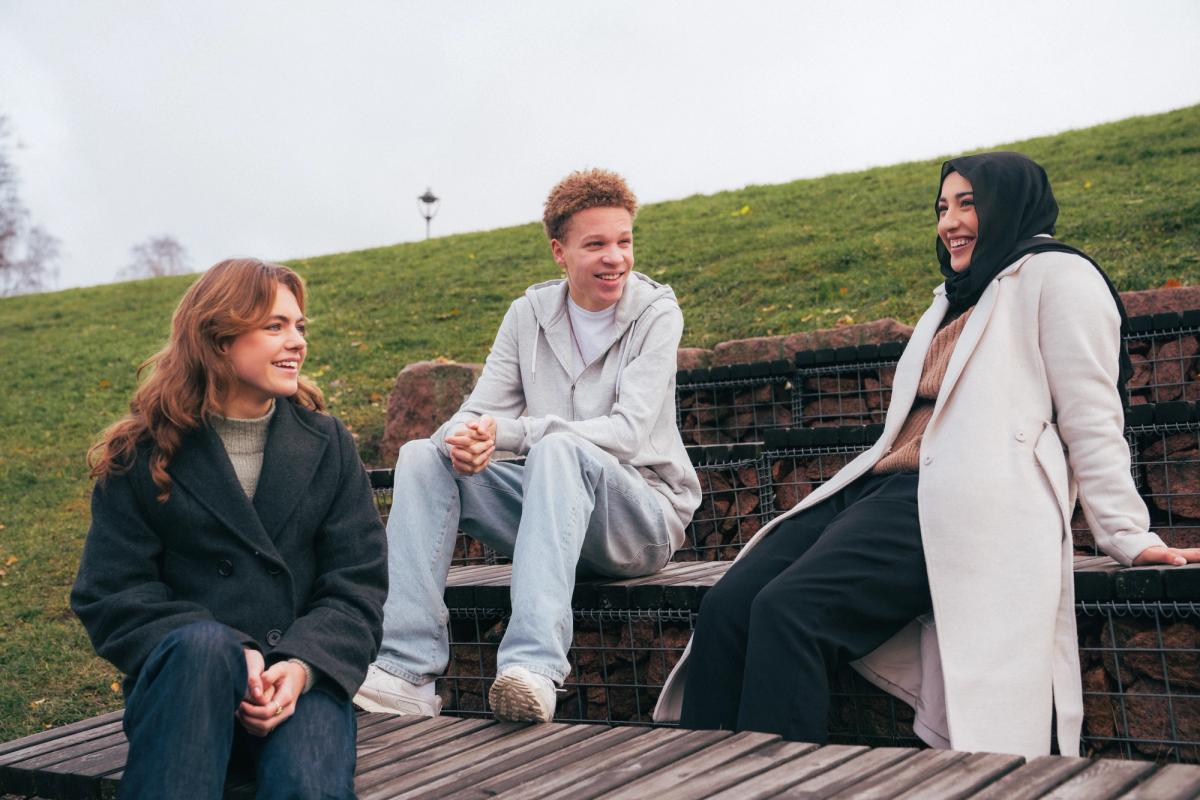 Tre ungdommer snakker og ler sammen i en park