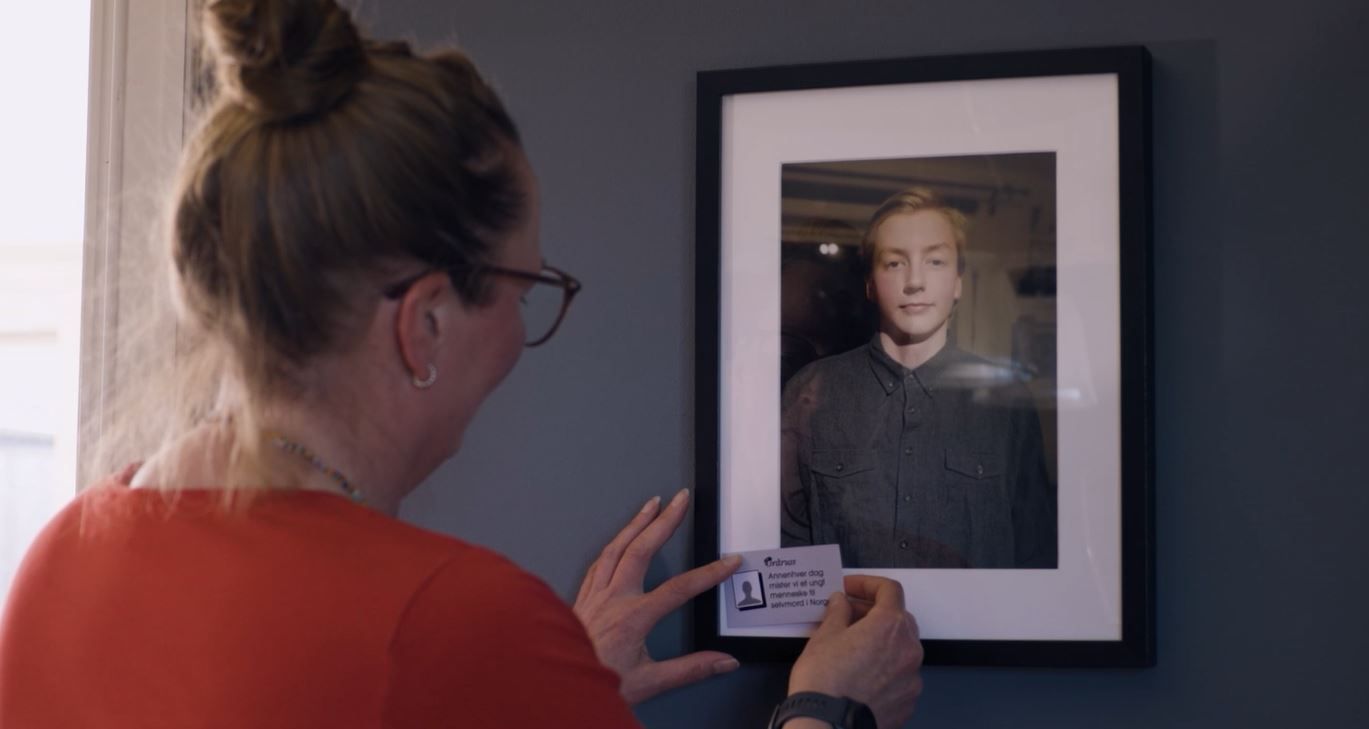 Mor til Elias står foran bilde å setter inn et grårussekort