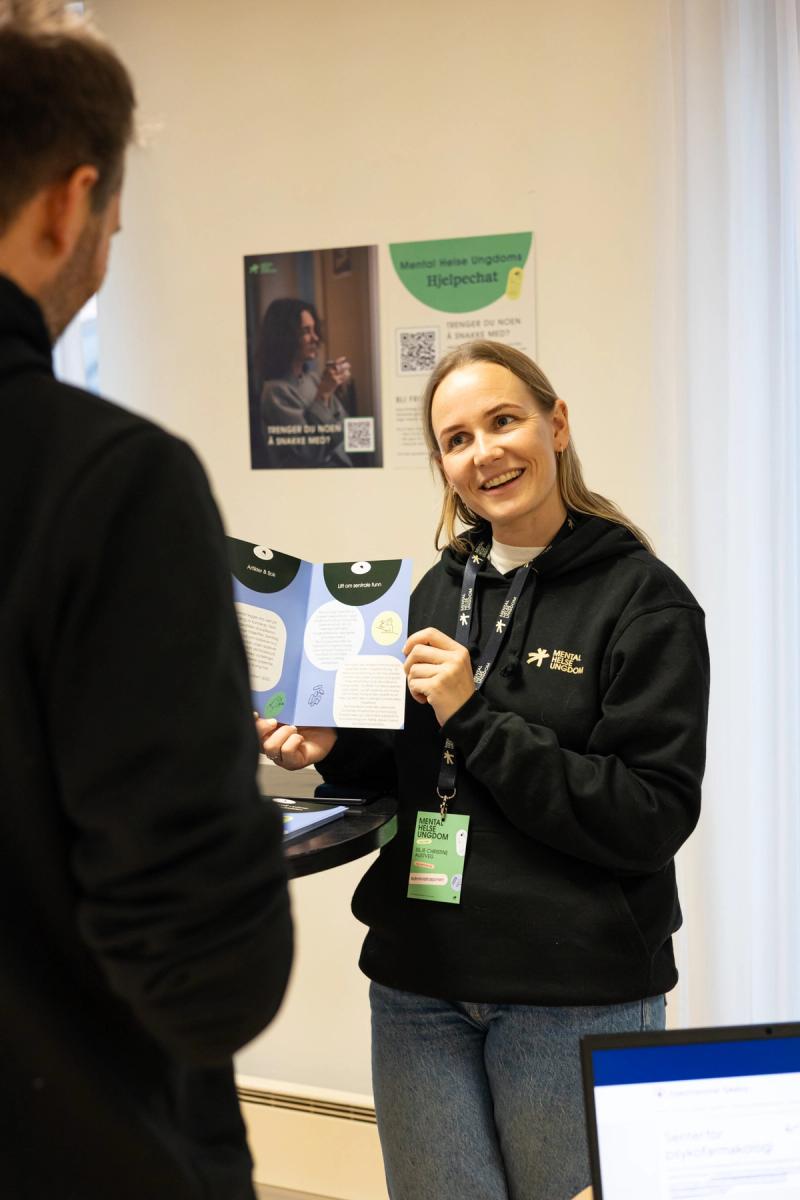 Person som står og viser frem med en brosjyre og smiler