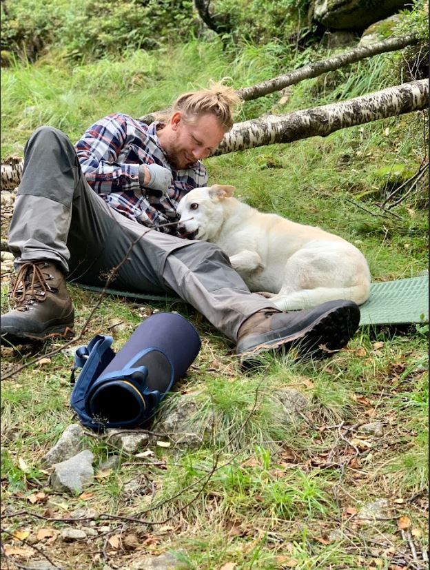 Fredrik som ligger på bakken mens en liten hund koser.